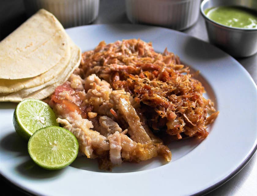 Un plato servido con carnitas tortillas y limón acompañadas de 3 salseros con cebolla cilantro y salsa verde en un restaurante de carnitas.