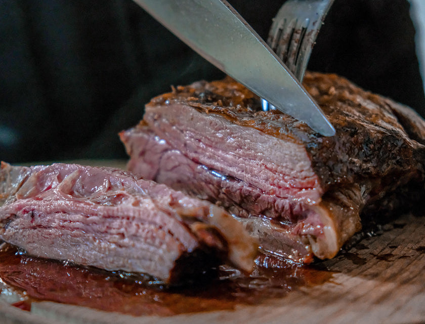 Un pernil asado siendo cortado con un cuchillo muy filoso sobre una tabla de madera por un mesero en un restaurante de pernil asado.