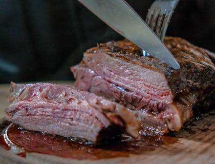 Un pernil asado siendo cortado con un cuchillo muy filoso sobre una tabla de madera por un mesero en un restaurante de pernil asado.
