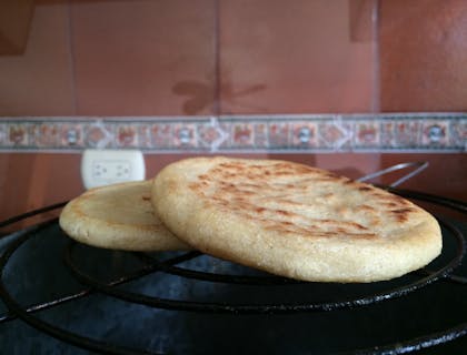 Dos arepas sobre una parrilla con una pared y un contacto eléctrico al fondo en un restaurante venezolano.