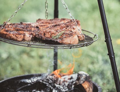 Tres cortes de carne asándose en una parrilla al aire libre fuera de un restaurante de parrillas.