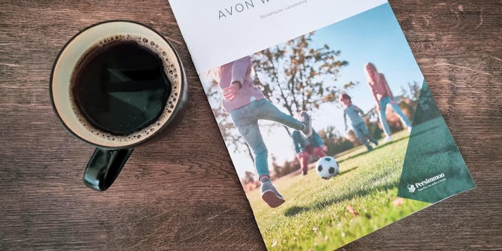 Una revista deportiva a un lado de un café negro sobre una mesa de madera oscura.