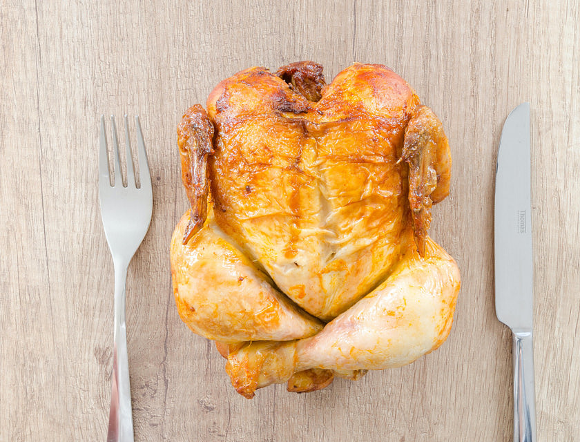 Un pollo rostizado en una mesa de madera con dos cubiertos a un lado en una rosticería.