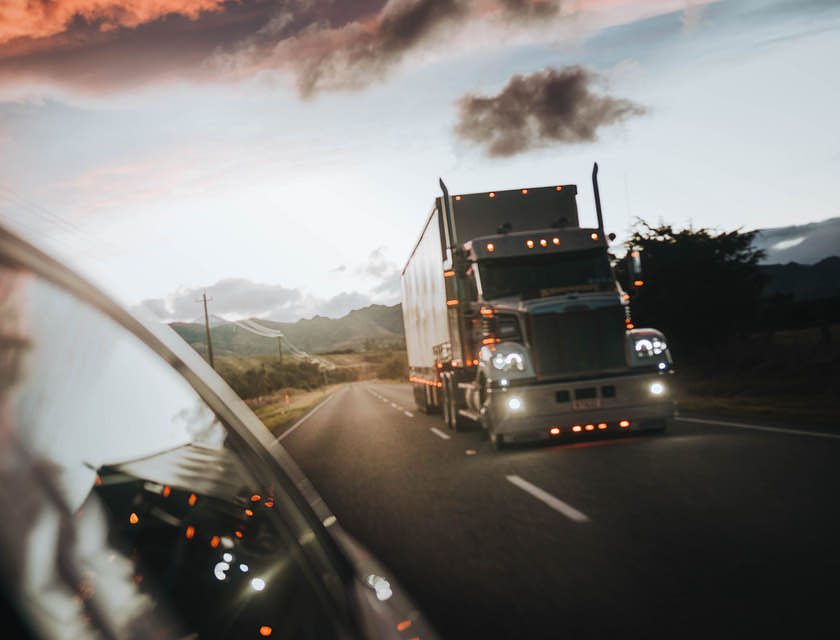 Vista de un tráiler de un servicio de fletes en la carretera con los faros encendidos.