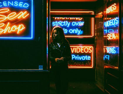 Una mujer usando una chamarra negra frente a una sex shop.