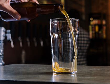 Una mano sirviendo sidra en un vaso en la barra de una sidrería.