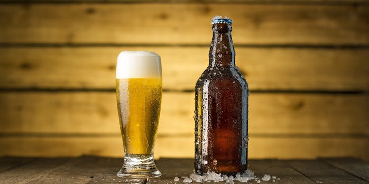 Um copo cheio e uma garrafa de cerveja geladas em cima de uma mesa de boteco