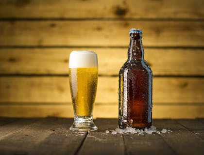 Um copo cheio e uma garrafa de cerveja geladas em cima de uma mesa de boteco