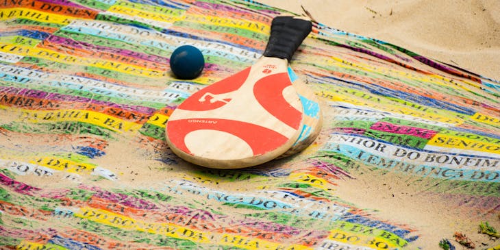 Duas raquetes e uma bolinha de frescobol em uma praia.