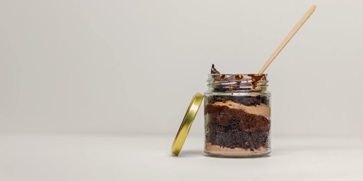 Um bolo no pote de chocolate e camadas de brigadeiro com um palito em cima.
