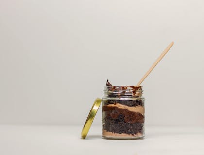 Um bolo no pote de chocolate e camadas de brigadeiro com um palito em cima.