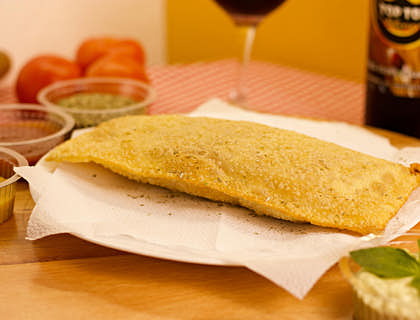 Um pastel em um prato em cima de uma mesa com molhos e uma taça de vinho.