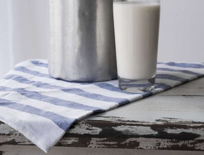 Un bicchiere di latte fresco e un bidone in alluminio per il latte.