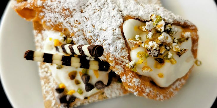 Un piatto bianco con un cannolo siciliano, dolce tipico della pasticceria siciliana.