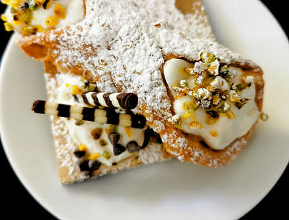 Un piatto bianco con un cannolo siciliano, dolce tipico della pasticceria siciliana.
