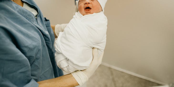 Baby being held by labor nurse in operating room.