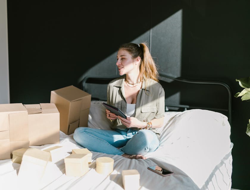 An online store business owner working on a tablet with boxes of items ready to be shipped.