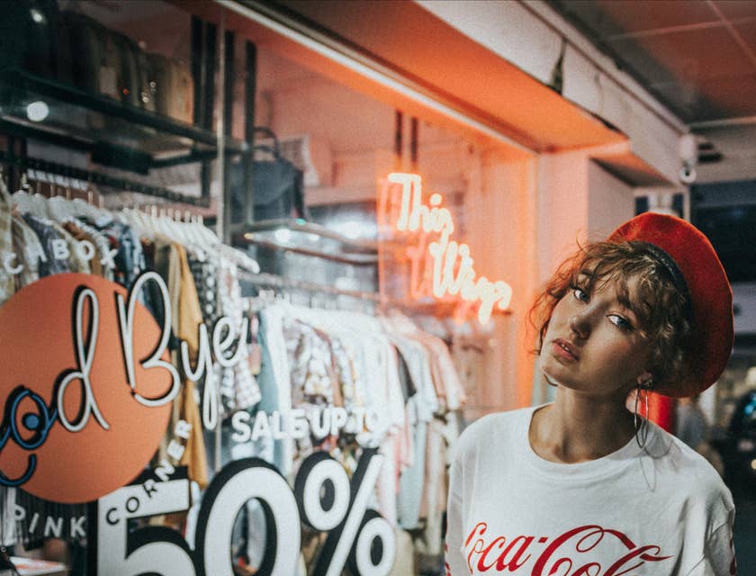 Une fille portant un t-shirt Coca-Cola et un béret rouge pose devant un magasin d'usine.