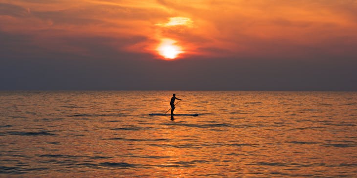 A person paddleboarding in the sea at sunset.
