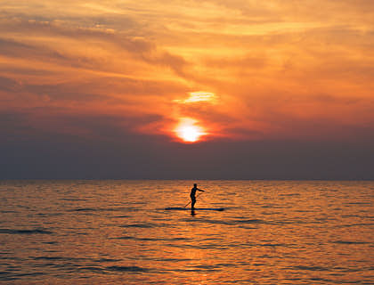 A person paddleboarding in the sea at sunset.