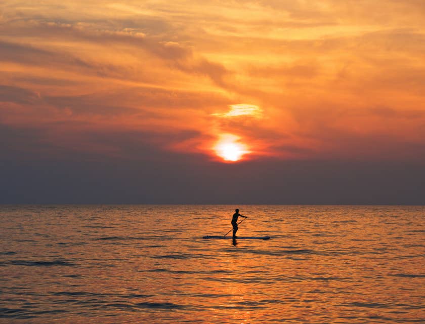 Una persona haciendo surf de remo en el mar al atardecer.