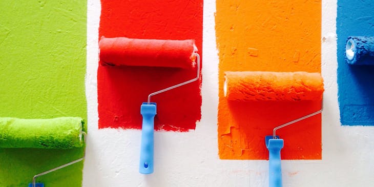 Four colors of paint being applied to the wall of a paint store by rollers.