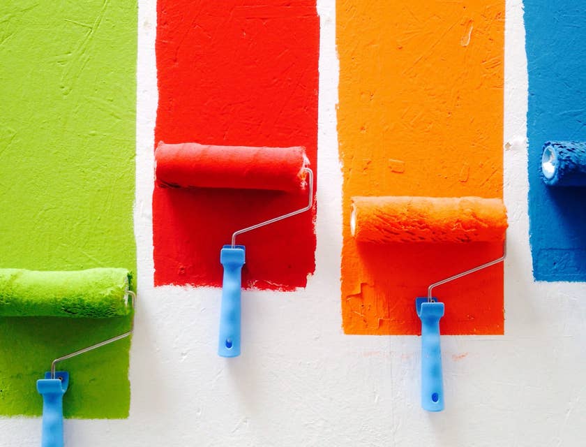 Quatro cores de tinta sendo aplicadas por rolos de pintura na parede de uma loja de tintas.