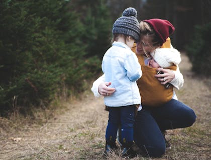 Une femme portant un bébé et parlant à un autre enfant plus âgé.