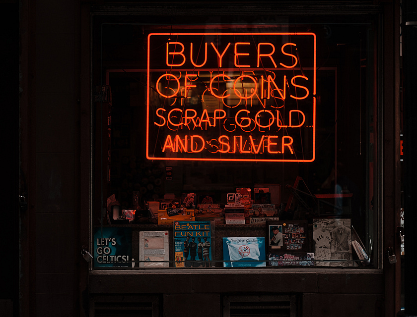 Die Fensterauslage eines Pfandhauses mit einer Neonleuchtreklame, in der Gold, Silber und Münzen beworben werden.