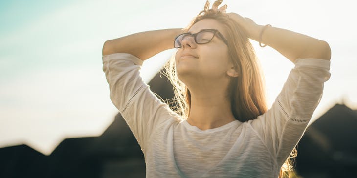 Femme aux yeux fermés, l'air paisible, faisant des étirements par une journée ensoleillée.