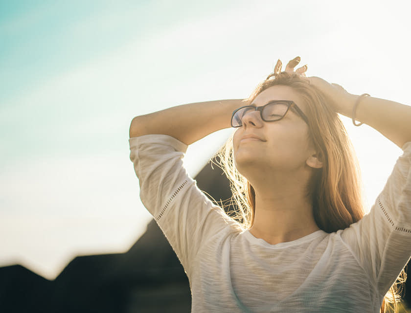 A woman with closed eyes looking peaceful while doing a stretch on a sunny day.