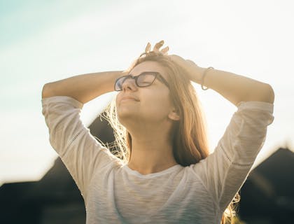 Mulher de olhos fechados se alongando em um dia ensolarado.