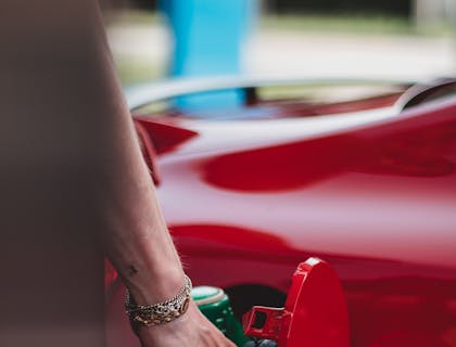 Pessoa abastecendo um carro vermelho com uma bomba de gasolina.