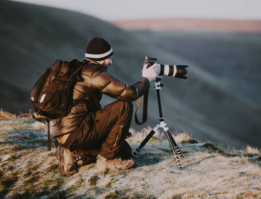 Un photographe accroupi au sommet d'une montagne en train de prendre des photos pour son entreprise de photographie.