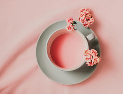 A cup of pink tea surrounded by flowers displayed against a pink background.