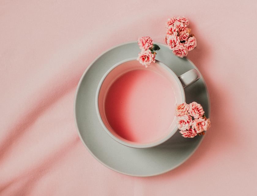 Une tasse de thé rose entourée de fleurs sur un fond rose.