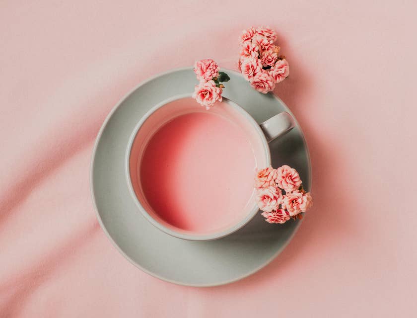 A cup of pink tea surrounded by flowers displayed against a pink background.
