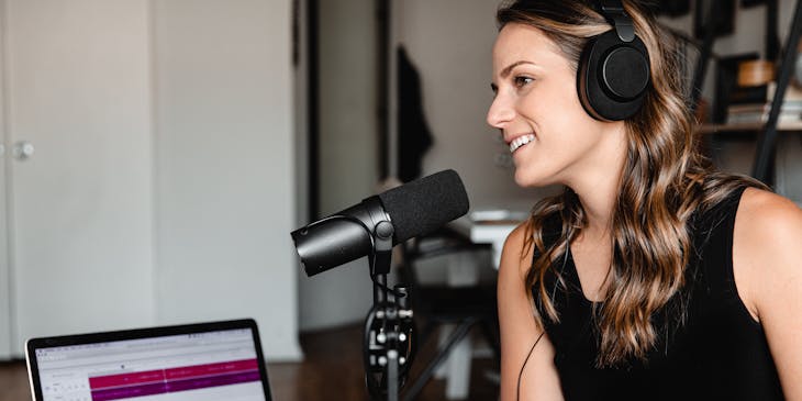 A woman with headphones and a microphone in a room recording a podcast.