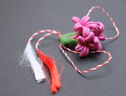 Eine modellierte, rosafarbene Blume aus Polymer-Ton an einem rot-weißen Faden.