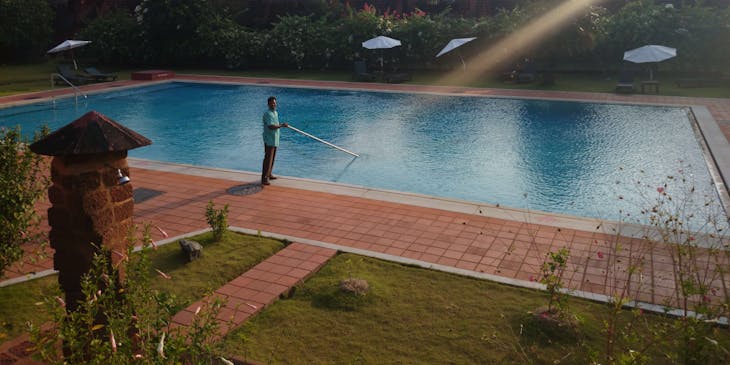 A man cleaning a large pool in a backyard.