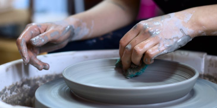 Person making a shallow clay bowl on a pottery wheel.