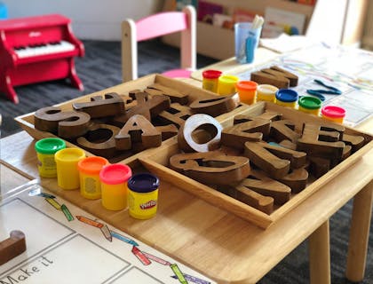 Children's desk set up with wooden alphabet pieces and colorful play doh sets at a preschool business.