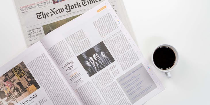 A print media newspaper and an open magazine besides a cup of coffee