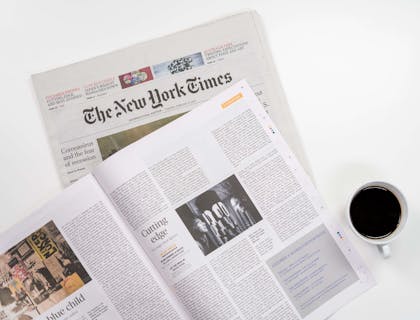 Un journal de la presse écrite et un magazine ouvert en plus d'une tasse de café.