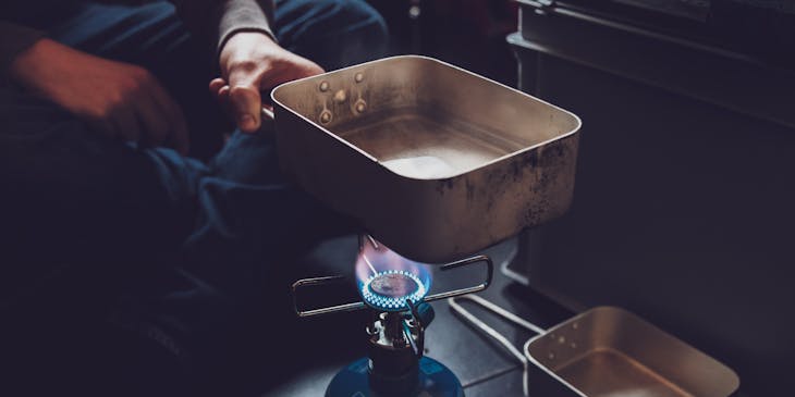 A man holding a pan over a propane flame.