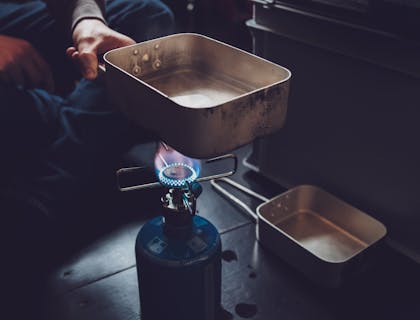 Eine Person hält eine Pfanne über eine Propangasflamme.