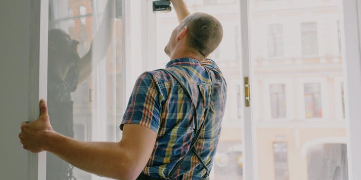 A handyman working for a property maintenance business installing a window in an apartment.