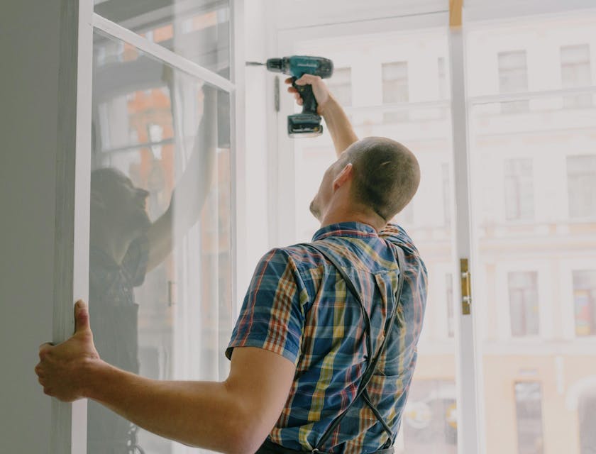 A handyman working for a property maintenance business installing a window in an apartment.