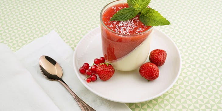 A strawberry and vanilla pudding displayed with a spoon on a white table.