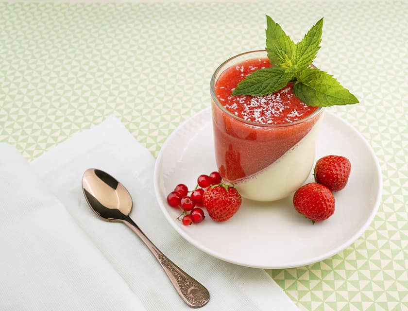 Un pouding aux fraises et à la vanille présenté avec une cuillère sur une table blanche.